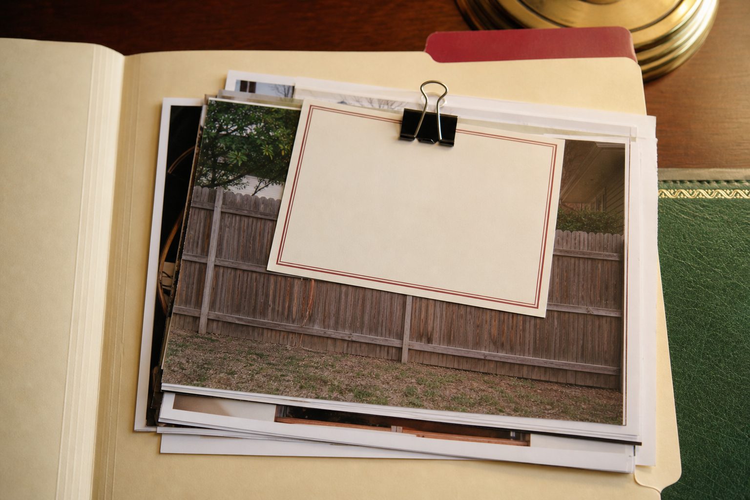 Open cream file folder with dated fence photos and a bordered notice card on a wooden desk